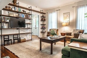 A living room with a television, bookshelves, a sofa, and a coffee table. - NEW! Downtown Charmer- Steps to downtown SoPines! (Southern Pines)
