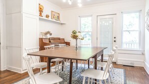 Ein Esszimmer mit Holztisch, weißen Stühlen, einem Klavier und einem Globus auf einem Regal.