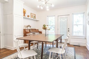 A dining room with a wooden table, white chairs, a piano, and a globe on a shelf. - NEW! Downtown Charmer- Steps to downtown SoPines! (Southern Pines)