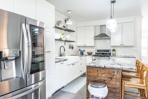 A modern kitchen with stainless steel appliances, white cabinetry, and a wooden island. - NEW! Downtown Charmer- Steps to downtown SoPines! (Southern Pines)