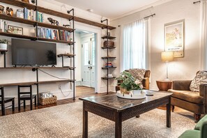 Un salon comprenant un téléviseur, des étagères à livres, une table basse, un canapé et une lampe.
