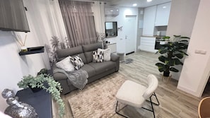 A modern living room with a grey sofa, a white chair, and a kitchen area in the background. - Villamadrid House, ideal for families, two vacation apartments, 7 minutes from the metro (villa de vallecas)