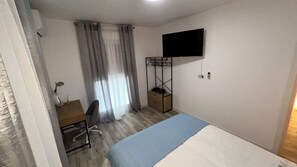 Ein Schlafzimmer mit Bett, Schreibtisch mit Stuhl, Wand-Fernseher und Kleiderständer.