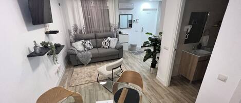 A modern living room with a sofa, coffee table, and chairs, a dining area with a table and chairs, and a kitchen with a sink and cabinets.