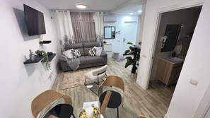 Ein modernes Wohnzimmer mit Sofa, Couchtisch und Sesseln, ein Essbereich mit Tisch und Stühlen sowie eine Küche mit Spüle und Schränken.
