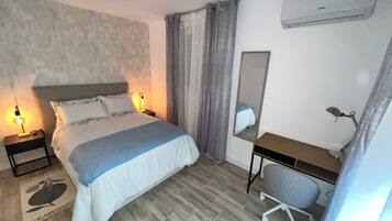 Quarto com cama, abajures, escrivaninha com cadeira, espelho e aquecedor.