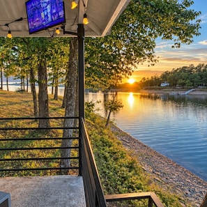 A lakeside view with a sunset, a dock, and a building with a TV screen. - Lakefront Home with Guest house, easy walk to dock and sand volleyball court (Crane Hill)