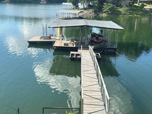 A dock extending into a lake with a covered seating area and a boat. - Lakefront Home with Guest house, easy walk to dock and sand volleyball court (Crane Hill)