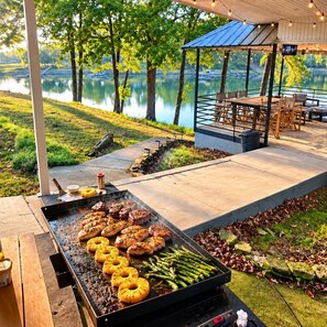 Een buitenbarbecue met eten, een overdekte zithoek en uitzicht op een meer.