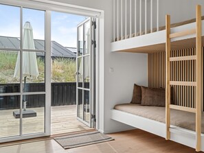 Et værelse med køjeseng, en skydedør til en udendørs terrasse og udsigt over naturen.