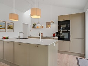 A modern kitchen with a central island, pendant lighting, and built-in appliances. - "Karoliina" - 500m from the sea by Interhome (Løkken)