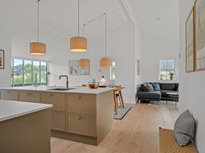 Une cuisine moderne dotée d’un îlot central, de luminaires suspendus et offrant une vue sur l’extérieur.