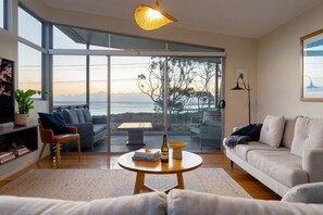A modern living room with a large sliding glass door leading to a balcony with a view of the sea. - 138 Tasman - Bicheno Accommodation (Bicheno)