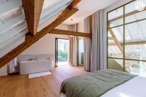 A bedroom with a large bed, a bathtub, and a balcony with curtains. - Maison Aluna - SAINT OFFENGE (SAINT OFFENGE)