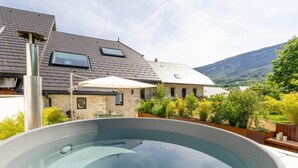 Uma piscina com um deck de pedra, uma casa de pedra com telhado inclinado e uma montanha ao fundo.