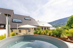 A swimming pool with a stone deck, a stone house with a sloped roof, and a mountain in the background. - Maison Aluna - SAINT OFFENGE (SAINT OFFENGE)