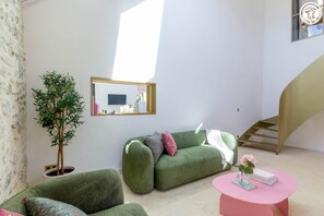 A modern living room with a green sofa, a pink table, and a potted plant. - Maison Aluna - SAINT OFFENGE (SAINT OFFENGE)