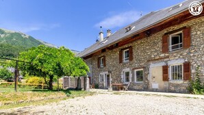 A stone building with a gravel driveway, wooden shutters, and a table with chairs outside. - The Priory Gardens (CLERY)