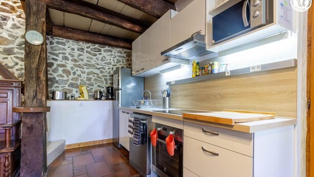 A kitchen with stone walls, wooden beams, a built-in oven, and a microwave. - The Priory Gardens (CLERY)