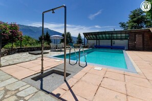A swimming pool with a metal frame, a covered seating area, and a stone patio. - The Priory Gardens (CLERY)