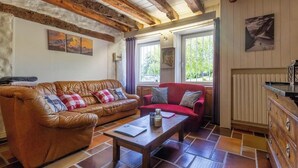 A cozy living room with a leather sofa, a red sofa, and a wooden coffee table. There are windows with curtains, a radiator, and a painting on the wall. - The Priory Gardens (CLERY)