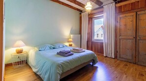 A bedroom with a bed, two bedside lamps, a window with curtains, and wooden walls. - The Priory Gardens (CLERY)