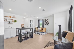 A modern kitchen with white cabinets, a dining table, and a living area with a sofa and a coffee table. - 2-bedroom house in peaceful Fort Worth with cool AC breeze (Fort Worth)