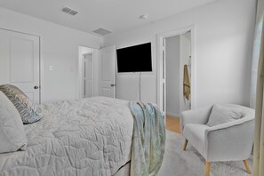 A bedroom with a bed, a TV mounted on the wall, a chair, and a door leading to another room. - 2-bedroom house in peaceful Fort Worth with cool AC breeze (Fort Worth)