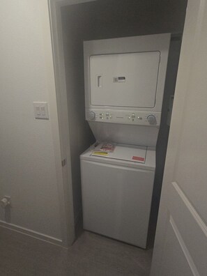 A compact laundry room with a front-loading washer and dryer, a control panel, and a QR code sticker. - 2-bedroom house in peaceful Fort Worth with cool AC breeze (Fort Worth)