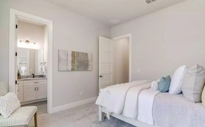 A bedroom with a bed, a chair, a door, and a bathroom visible through an open door. - Enjoyable 3-bedroom building with AC in welcoming Mattapoisett (Mattapoisett)