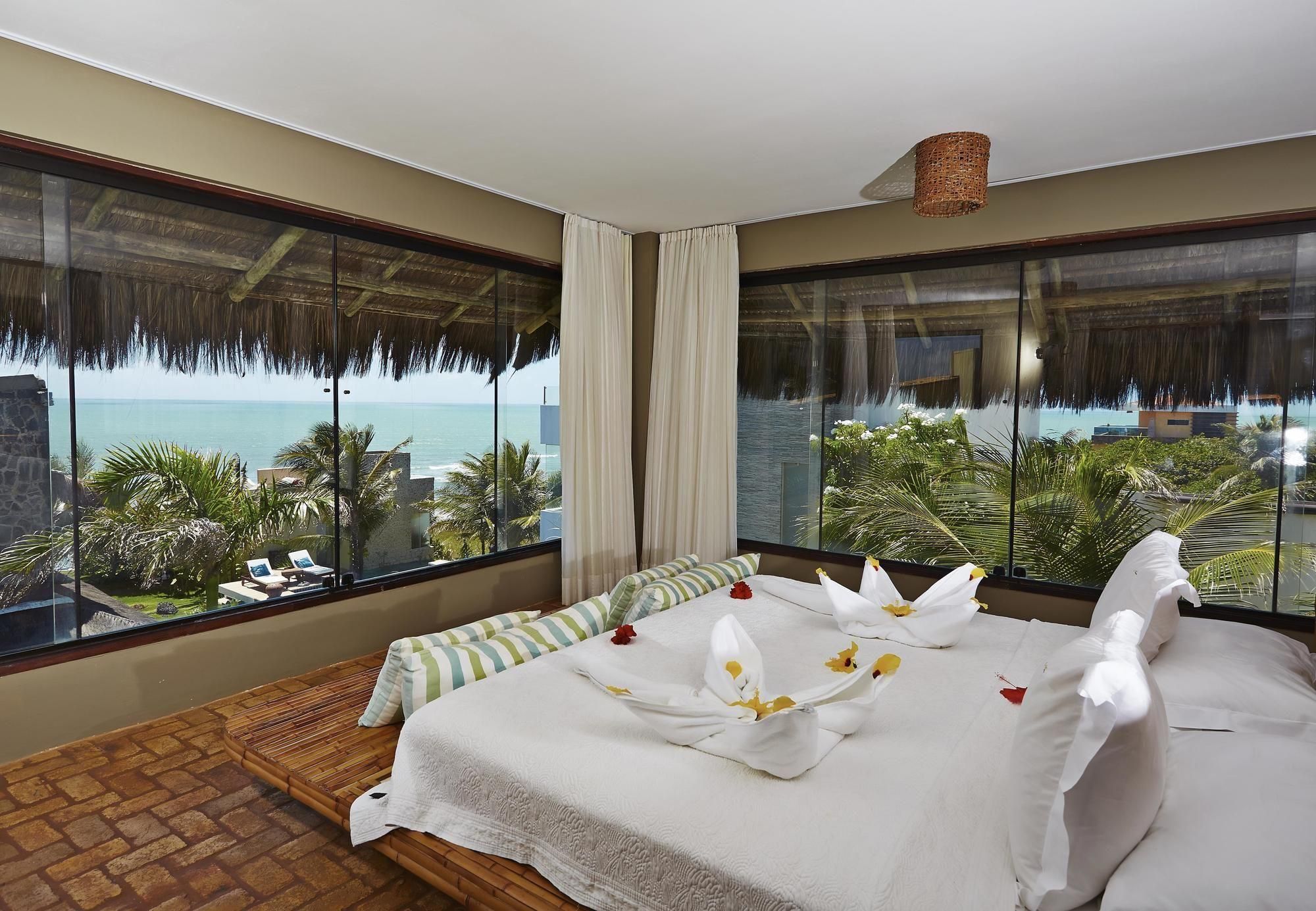 Quarto de hotel com uma cama grande, vista para o oceano e varanda com telhado de palha.