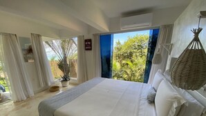 A bedroom with a large bed, a view of greenery outside, and a hanging basket. - Kilombo Villas And Spa (Tibau do Sul)