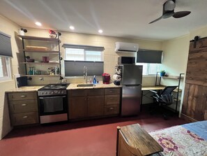 Eine kleine Küche mit Herd, Spüle und Kühlschrank, einem Deckenventilator und einem Fenster mit Jalousien.
