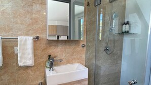 A modern bathroom with a glass-enclosed shower, a white sink, and a wooden vanity. - Private studio near street (Padstow)