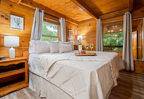 Dormitorio de cabaña de madera con una cama grande, lámparas de noche, mesita de noche y una ventana con cortinas.
