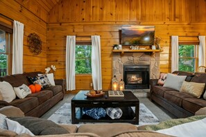 A cozy log cabin interior with two sofas, a fireplace, and a large window. - Family Cabin ✨️ Hot Tub ✨️ Game Room ✨️ 2 Mi to The Island✨️ 5 Mi to Dollywood (Pigeon Forge)