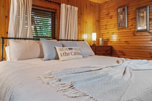 A wooden-paneled bedroom with a bed, pillows, a blanket, and a nightstand with a lamp. - Family Cabin ✨️ Hot Tub ✨️ Game Room ✨️ 2 Mi to The Island✨️ 5 Mi to Dollywood (Pigeon Forge)