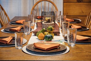 Una mesa de comedor dispuesta con platos, vasos y un centro de mesa decorado con calabazas.