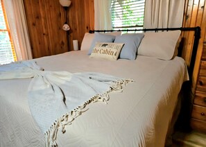Een bed met een witte dekbedovertrek, een plaid en een kussen met een ontwerp gebaseerd op een blokhut.