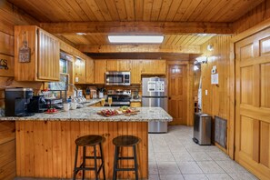 A wooden cabin kitchen with a central island, bar stools, a coffee maker, and a refrigerator. - Family Cabin ✨️ Hot Tub ✨️ Game Room ✨️ 2 Mi to The Island✨️ 5 Mi to Dollywood (Pigeon Forge)