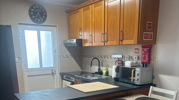 A kitchen with wooden cabinets, a built-in stove, a microwave, and a dining table with chairs. - Casa da Maré - a cozy atmosphere with a view of the ocean (Calheta)