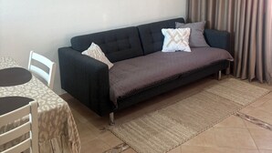 A living room with a dark sofa, a patterned rug, a dining table with chairs, and three wall-mounted decorative items. - Casa da Maré - a cozy atmosphere with a view of the ocean (Calheta)