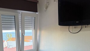 A bedroom with a bed, a TV mounted on the wall, a window with blinds, and a view of the sea. - Casa da Maré - a cozy atmosphere with a view of the ocean (Calheta)