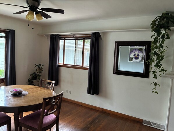 A dining area with a round table, chairs, a ceiling fan, a window with curtains, and a wall-mounted plant.