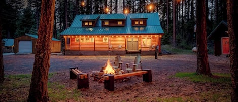 A cabin with a fire pit, wooden deck, and a porch with string lights.