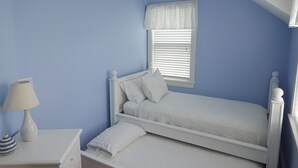 Um quarto com uma cama de solteiro, uma mesa de cabeceira com abajur e uma janela com persianas.