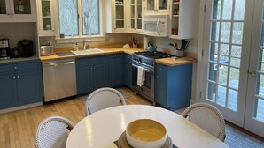 Uma cozinha moderna com armários azuis, bancada branca e um espaço de refeições com cadeiras de vime.