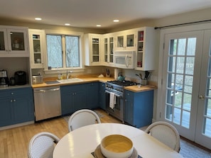 A modern kitchen with blue cabinets, a white countertop, and a dining area with wicker chairs. - Charming 4-bedroom house in Miacomet (Nantucket)