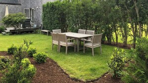 Um quintal residencial com um deck de madeira, uma mesa de jantar com cadeiras e um gramado bem cuidado.