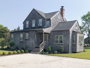Une maison à deux étages avec un porche à l’avant, une cheminée et une allée gravillonnée.